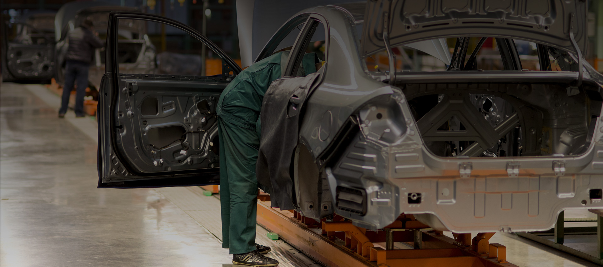 Photograph of the inside of a car manufacturing facility, with a worker working on the inside of the car